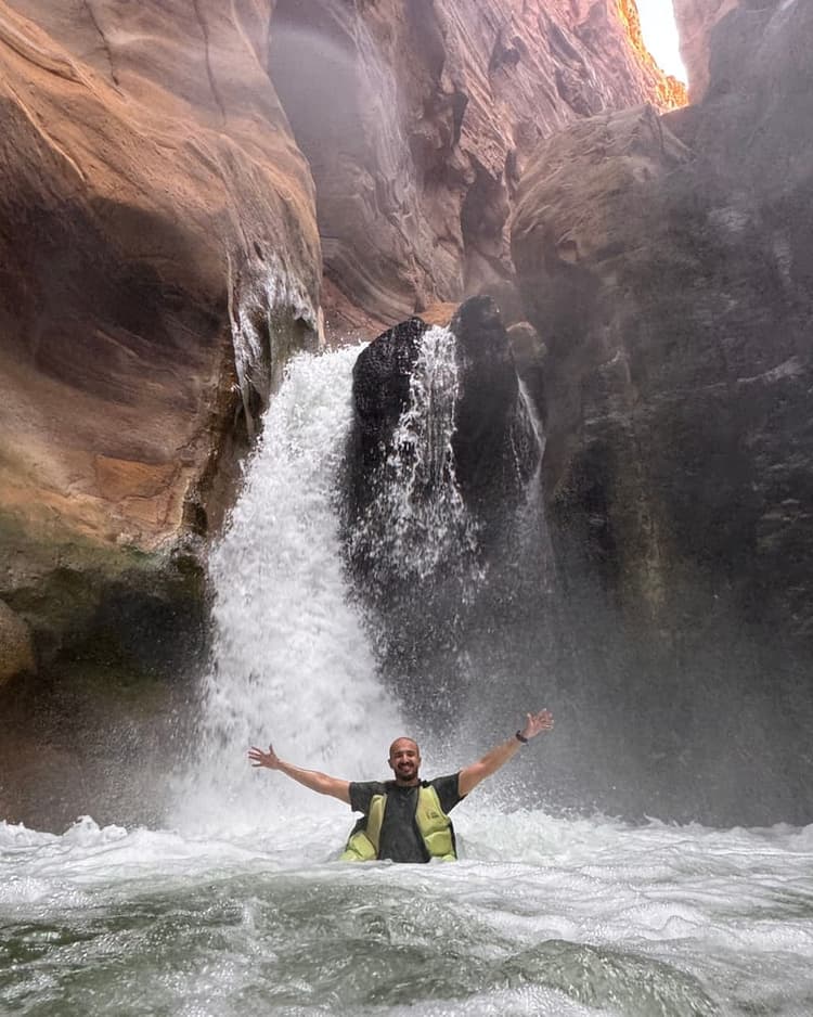 A waterfall in a red-rock canyon, with Abdulrahman in the pool below it
